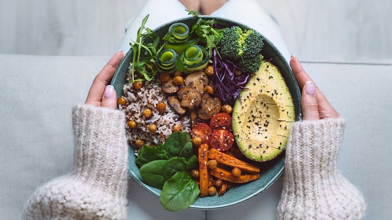Zwei Frauenhände halten einen Teller mit veganer Nahrung, die vegane Nahrungsergänzung braucht.