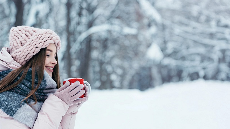 Frau mit Tasse im Schnee, die Wintermüdigkeit bekämpfen möchte
