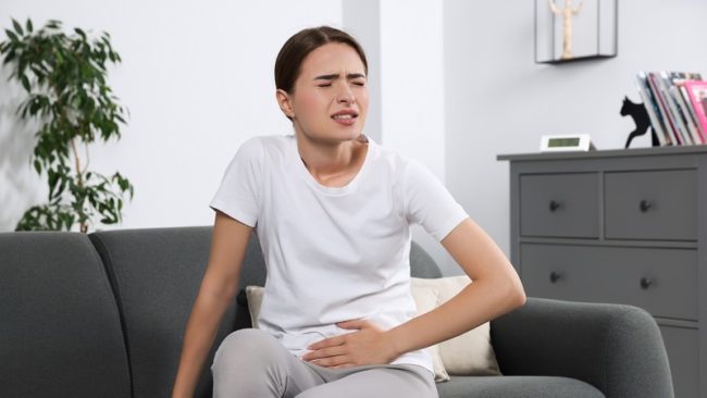 Eine Frau mit einer Blasenentzündung greift sich mit ihrer linken Hand auf den Bauch.