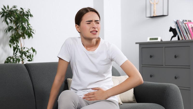 Eine Frau mit einer Blasenentzündung greift sich mit ihrer linken Hand auf den Bauch.