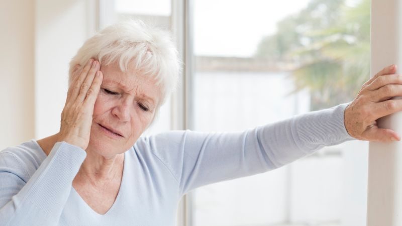 Person, die sich an Wand festhält und sich an den Kopf greift