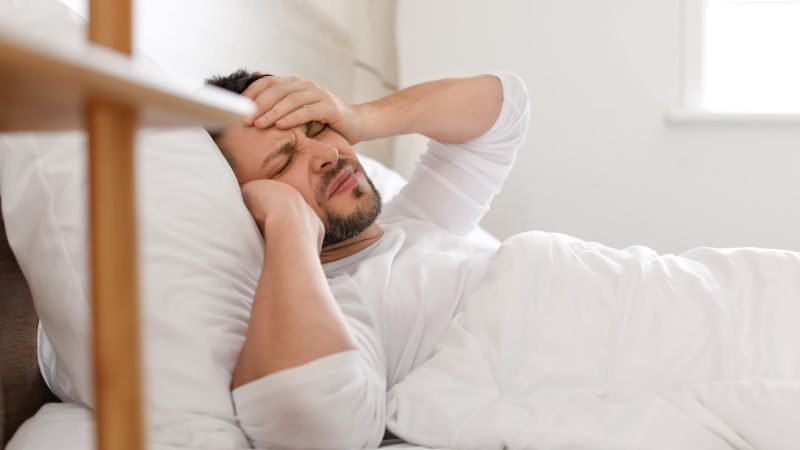 Person, die im Bett liegt und sich genervt den Kopf reibt