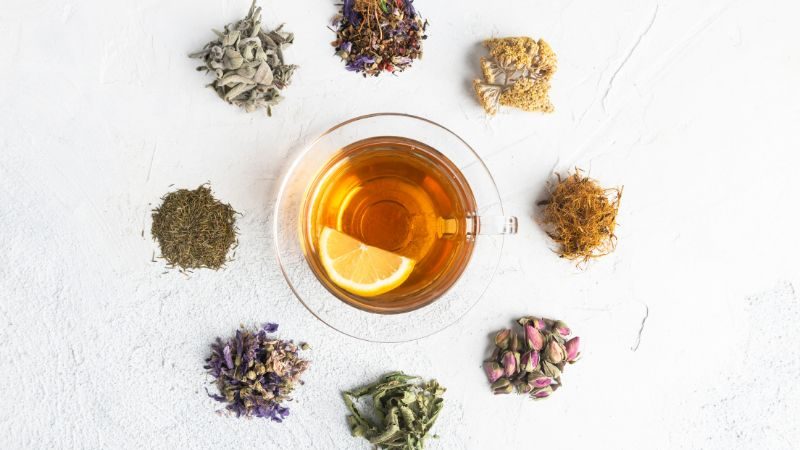 Tasse Tee umgeben von verschiedenen Teekräutern